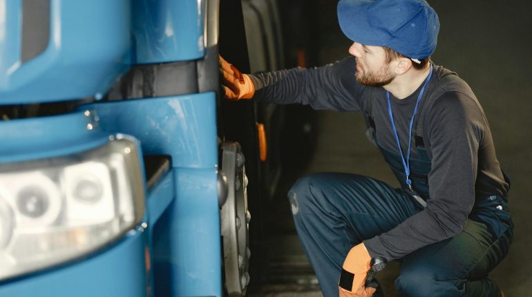 Mechaniker prüft Radkasten eines blauen LKW vor einer Auktion für Nutzfahrzeuge.