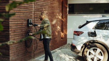 Person verbindet ein Elektroauto mit einer Wallbox an einer Holzwand