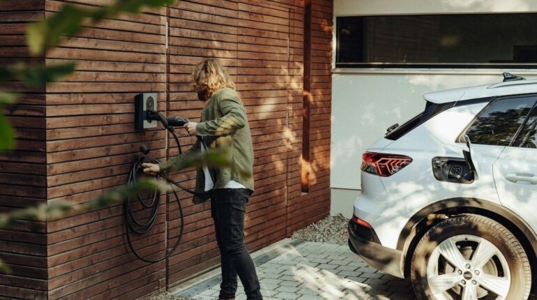 Person verbindet ein Elektroauto mit einer Wallbox an einer Holzwand